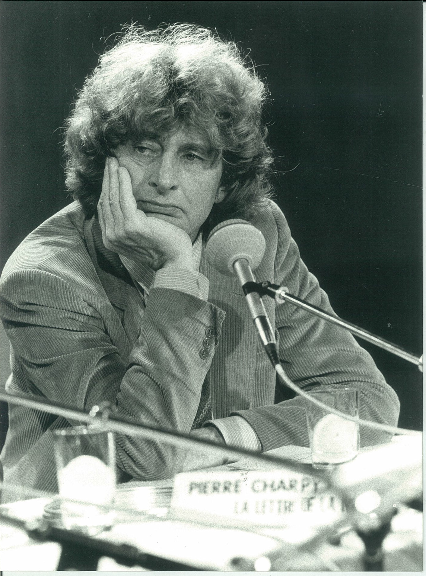 Paul Guilbert derrière une table de conférence avec plusieurs micros. Photo en noir et blanc.