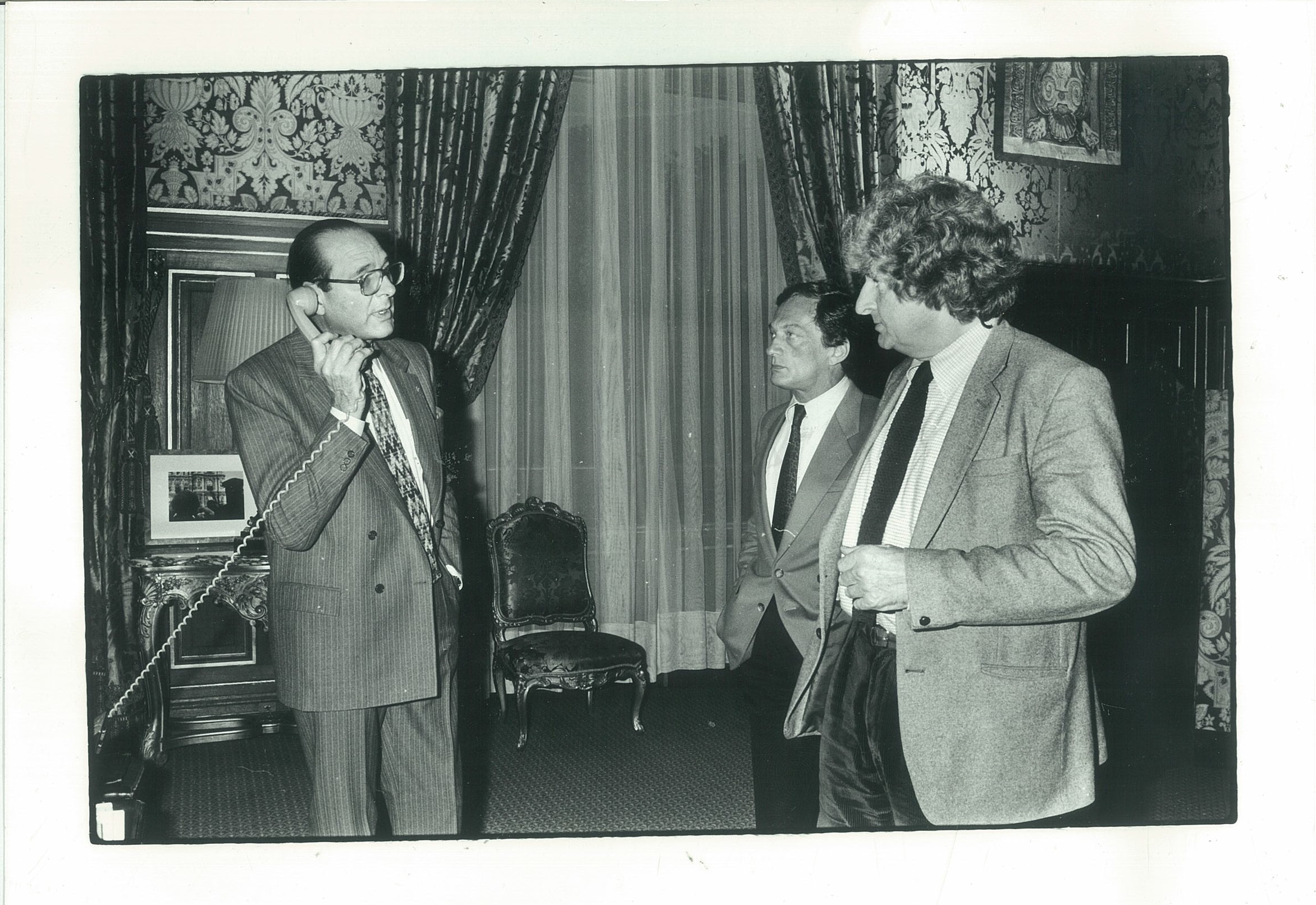 Jacques Chirac, Philippe Tesson et Paul Guilbert à l'Hôtel de Ville de Paris. Jacques Chirac téléphone. Photo en noir et blanc.
