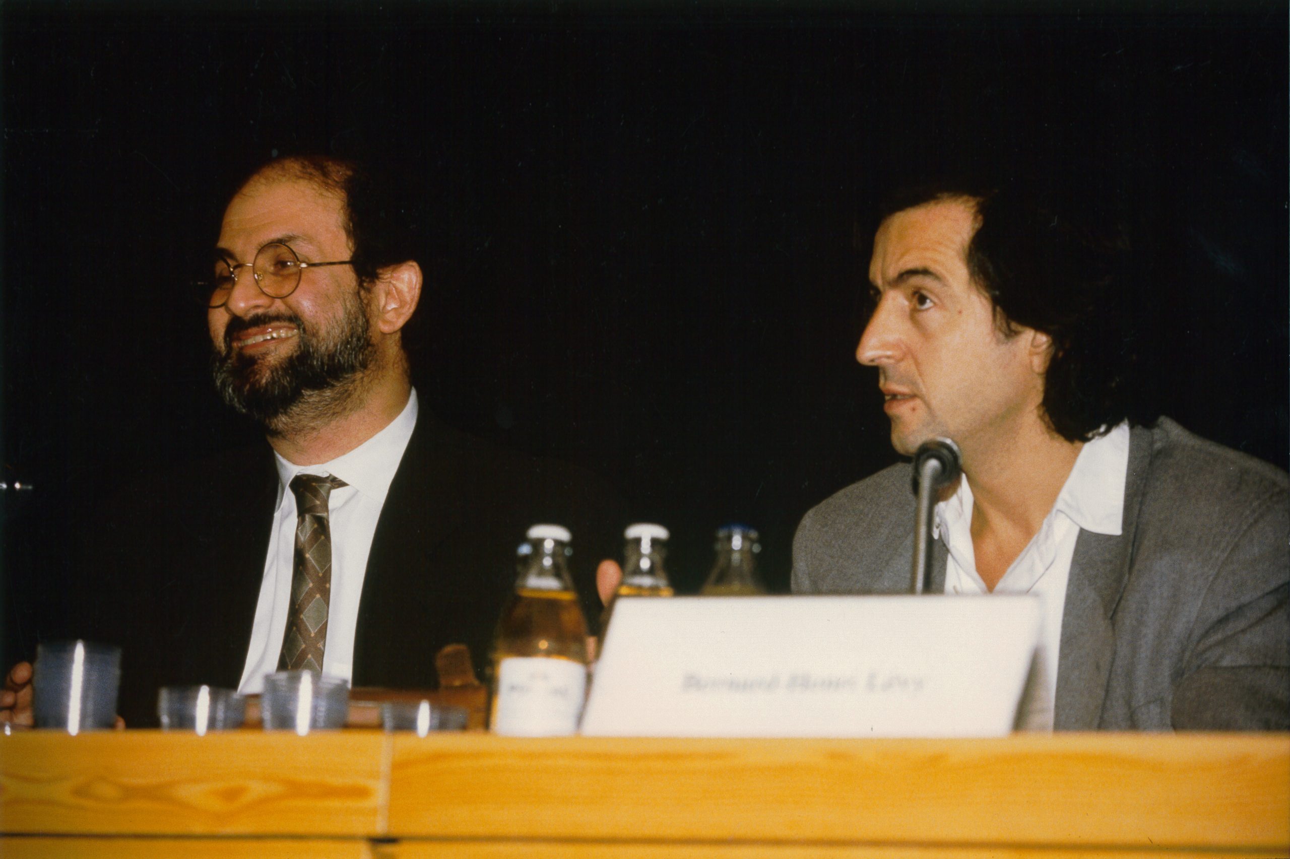 Bernard-Henri Lévy et Salman Rushdie assis derrière une table de conférence.