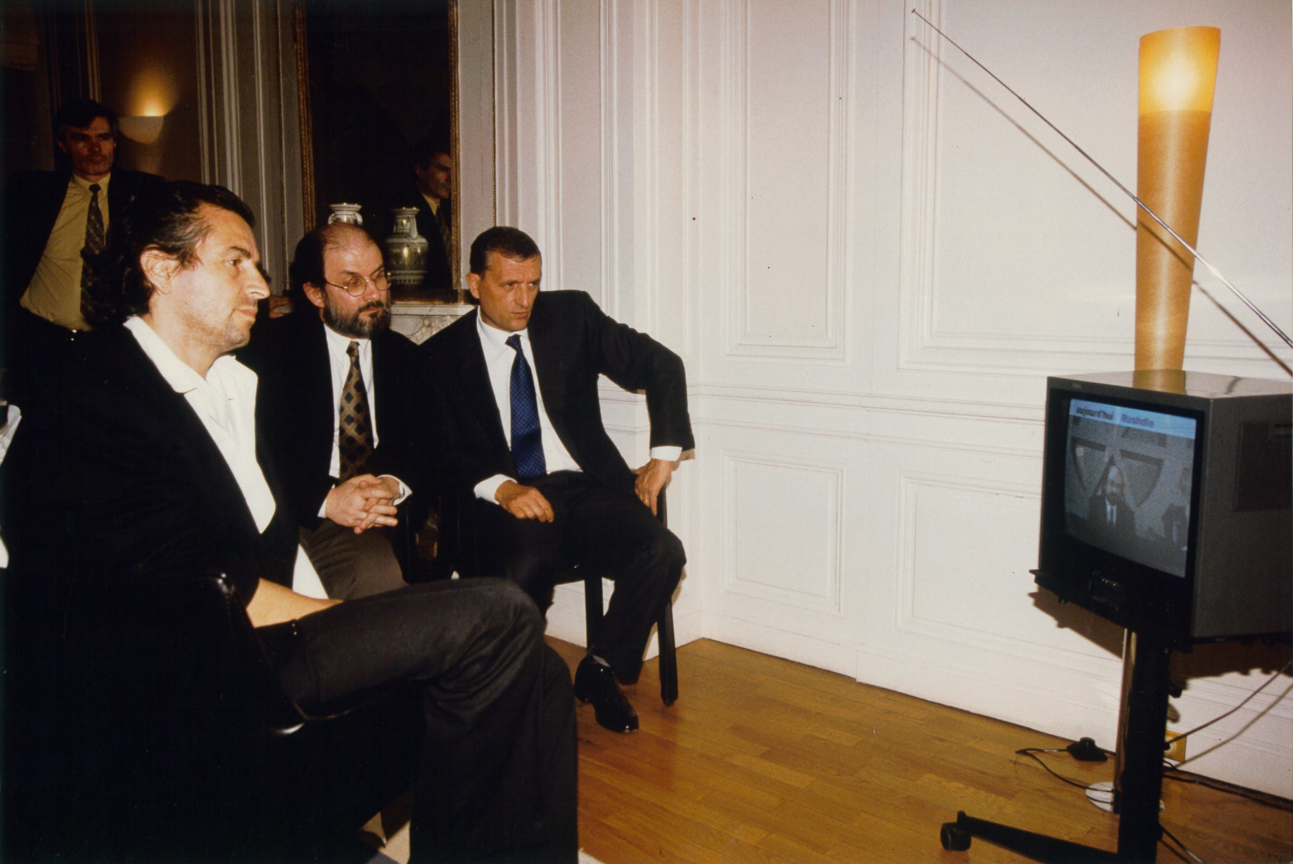 Bernard-Henri Lévy et Salman Rushdie assis devant un poste de télévision qui diffuse des images de Salman Rushdie.