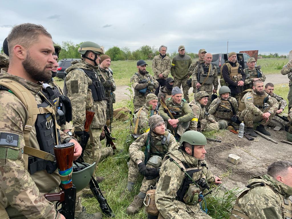 Bernard-Henri Lévy, en veste treillis, au milieu des membres du groupe Mozart en tenue militaires, au milieu de la campagne ukrainienne.
