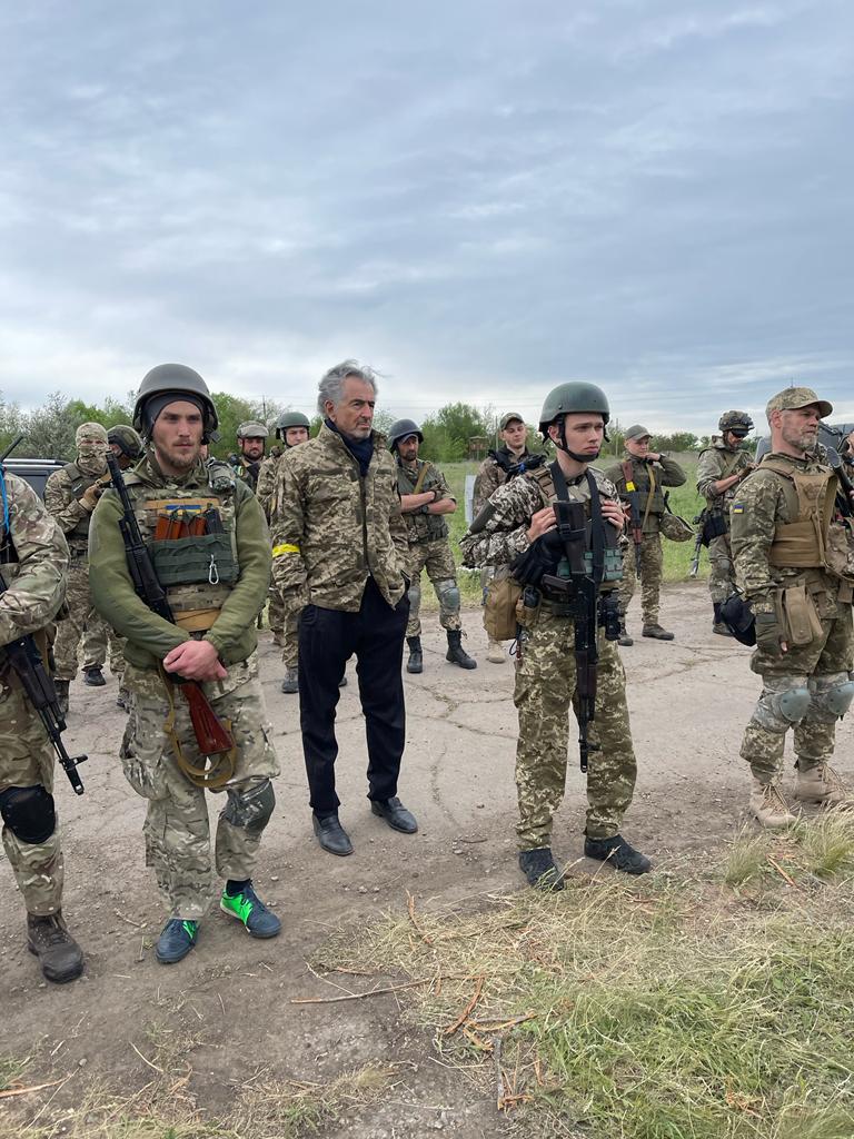 Bernard-Henri Lévy, en veste treillis, au milieu des membres du groupe Mozart en tenue militaires, au milieu de la campagne ukrainienne.