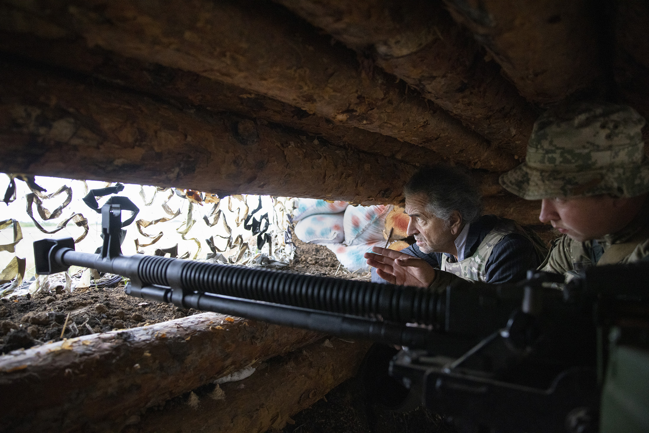 Bernard-Henri Lévy avec un militaire qui tient un arme lourde dans un abri de combat sur le front ukrainien.