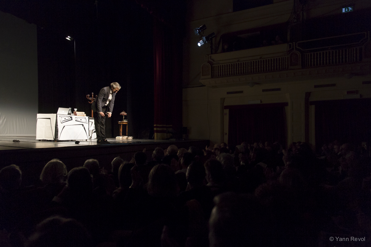 Seul à l'avant d'une scène de théâtre, Bernard-Henri Lévy salue le public.