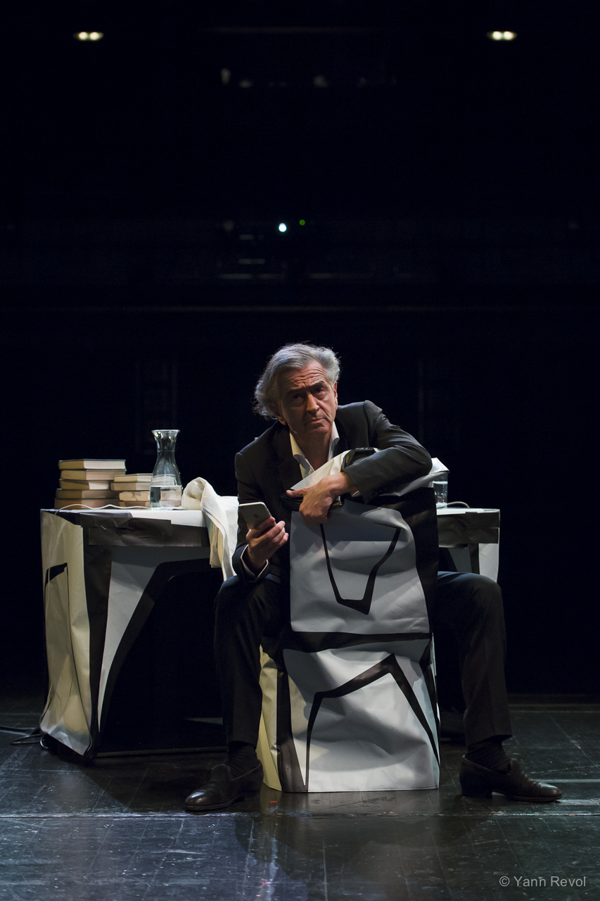 Bernard-Henri Lévy lors d'une répétition de sa pièce « Looking for Europe » au Theater Akzent de Vienne. Il est assis sur une chaise derrière un bureau, sur la scène du théâtre.