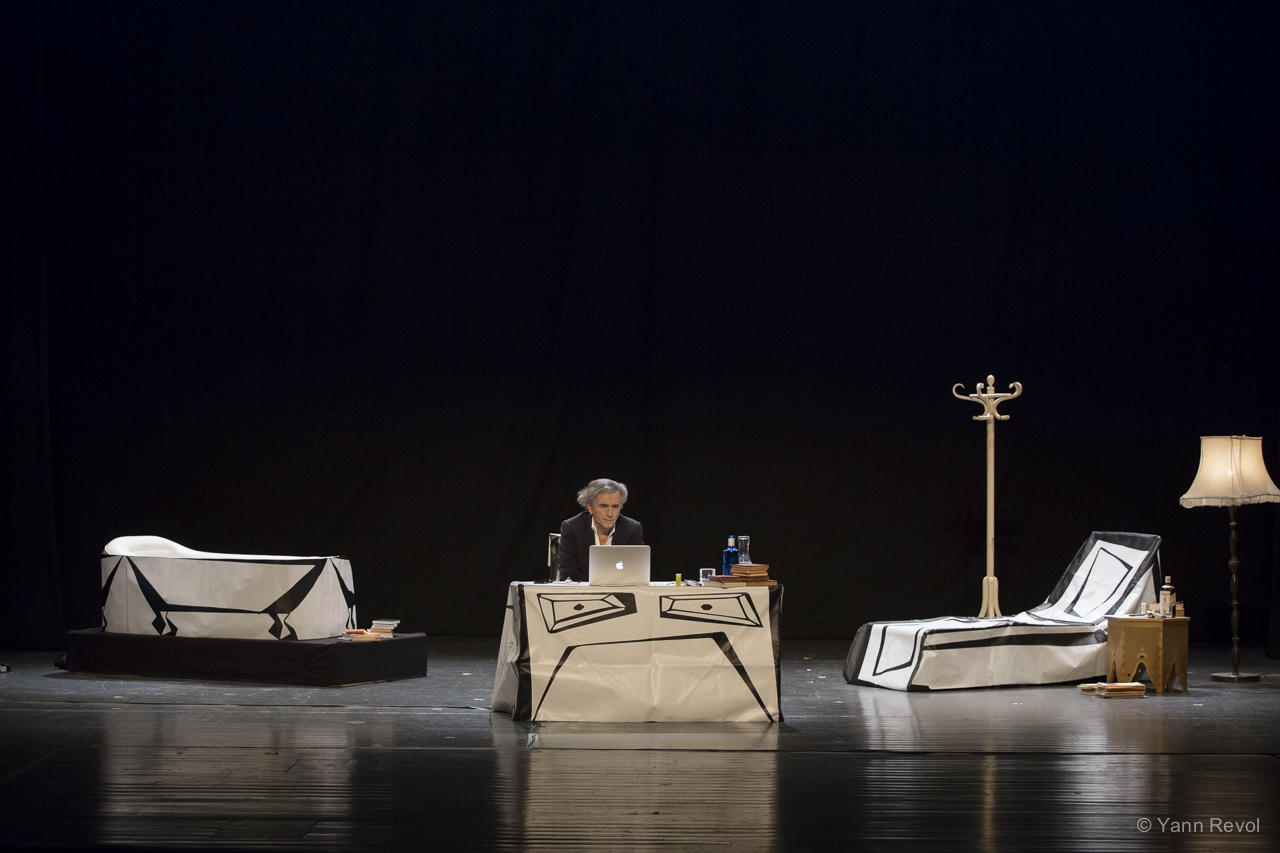 Bernard-Henri Lévy joue « Looking for Europe » à Sarajevo en Bosnie. Il est assis derrière un bureau sur la scène du Théâtre National. Dans le décor il y a un divan à droite, une baignoire à gauche.