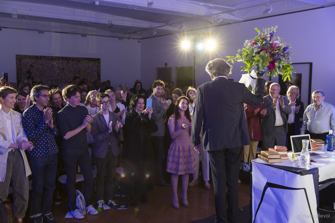 Bernard-Henri Lévy seul à l'avant scène il salue son public en portant un bouquet de fleurs.