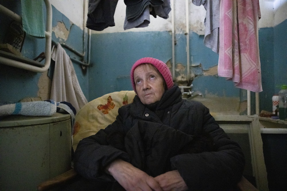 Femme âgée dans son appartement à Kiev, elle porte une doudoune et un bonnet.