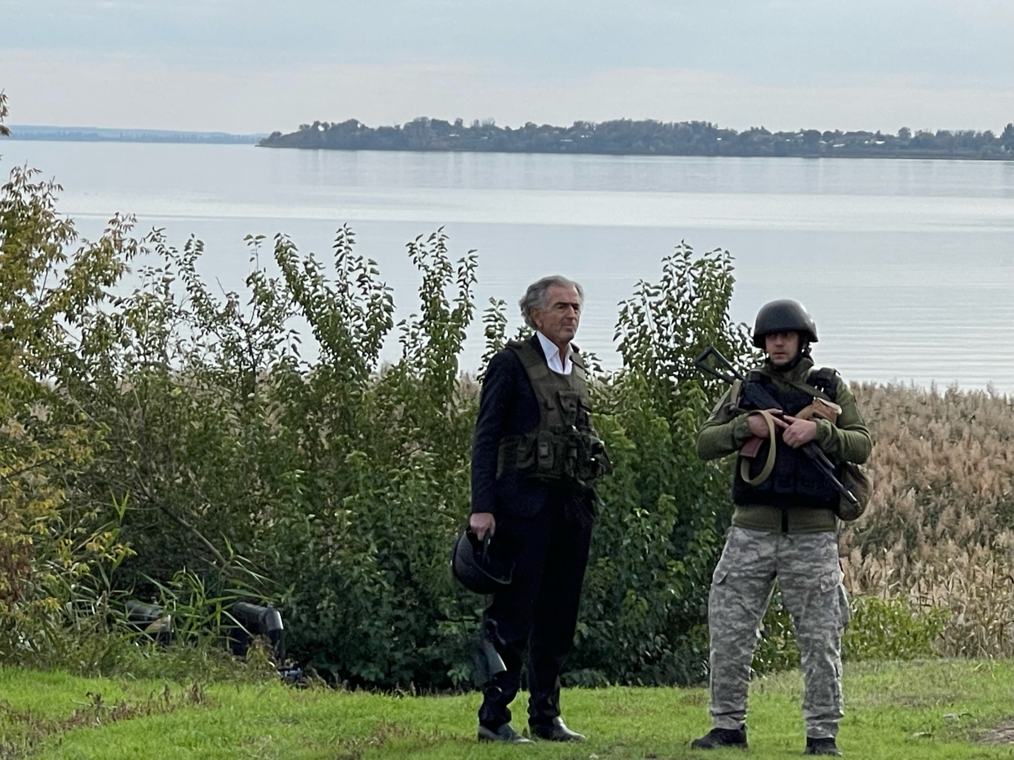 Bernard-Henri Lévy aux abords de la centrale de Zaporijjia, il est debout au bord de l'eau avec un militaire ukrainien.