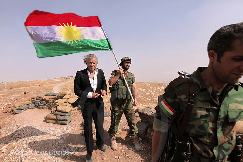 BHL dans le désert du Kurdistan, sur le front. Un militaire à côté de BHL porte un drapeau du Kurdistan irakien