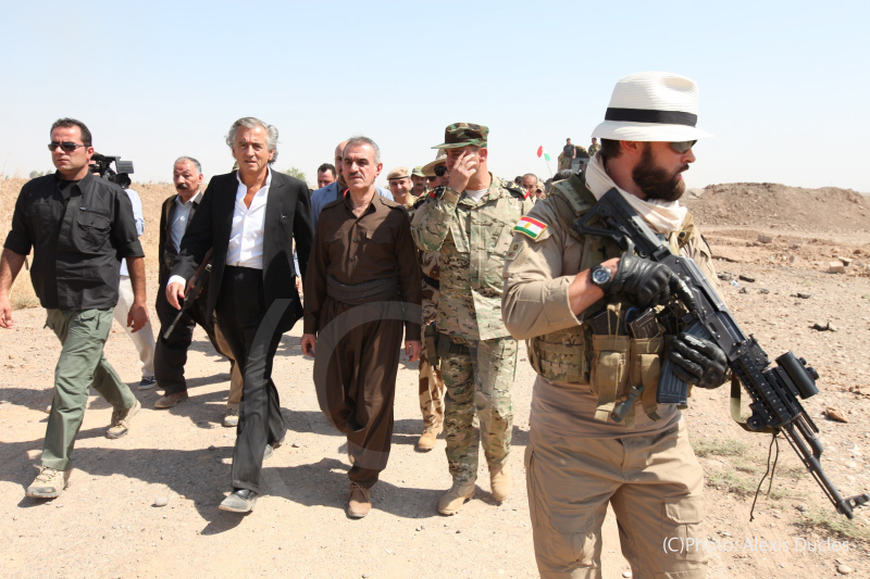 En août 2015 BHL se rend à Kurdistan irakien, auprès des Peshmergas. BHL est entouré part des militaires, ils marchent au milieu d'une route près d'un char de combat.