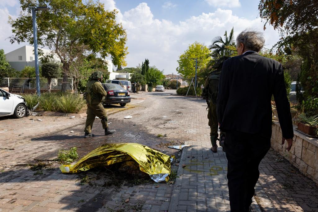 BHL marche dans une rue du Kibboutz de Kfar Aza avec un soldat. Il passe à côté de corps recouverts par une couverture de survie.