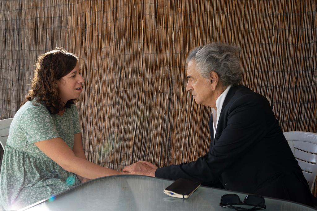 Bernard-Henri Lévy visite les kibboutzim d'Israël après le 7 Octobre, et se rend auprès des familles de victimes. Il est assis en face d'une femme à qui il tient la main.