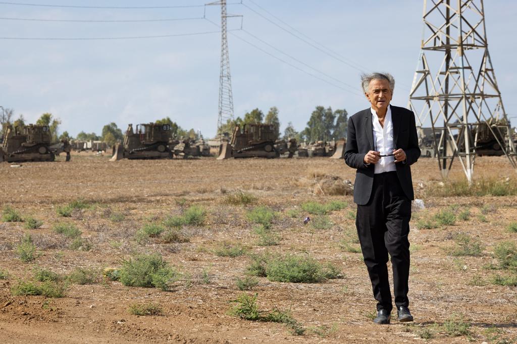 Bernard-Henri Lévy marche dans un champ. Derrière lui on voit Les unités de Tsahal positionnées au bord de la bande de Gaza qui se préparent à entrer en action.