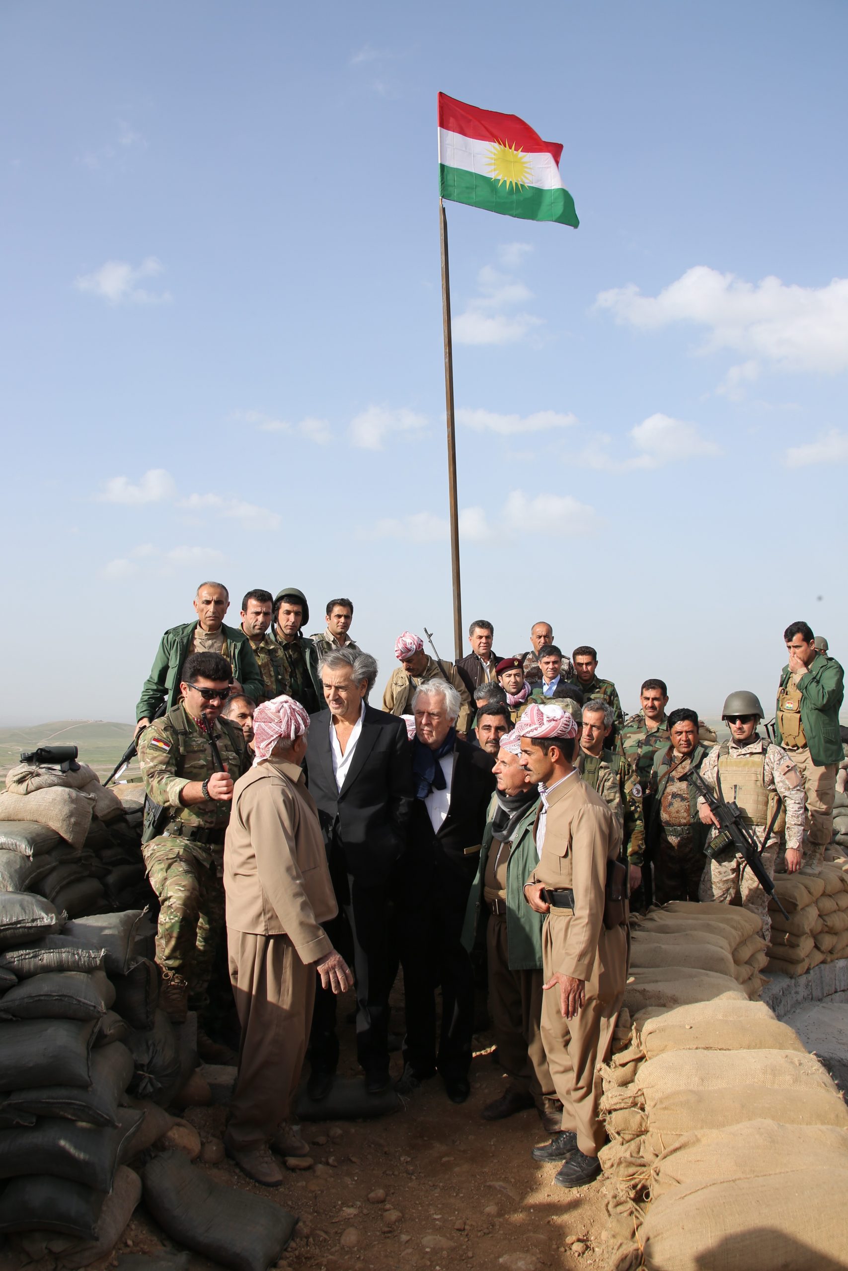 Bernard-Henri Lévy et Gilles Hertzog au Kurdistan irakien, avec les combattants Peshmergas, ils posent sous un drapeau du Rojava