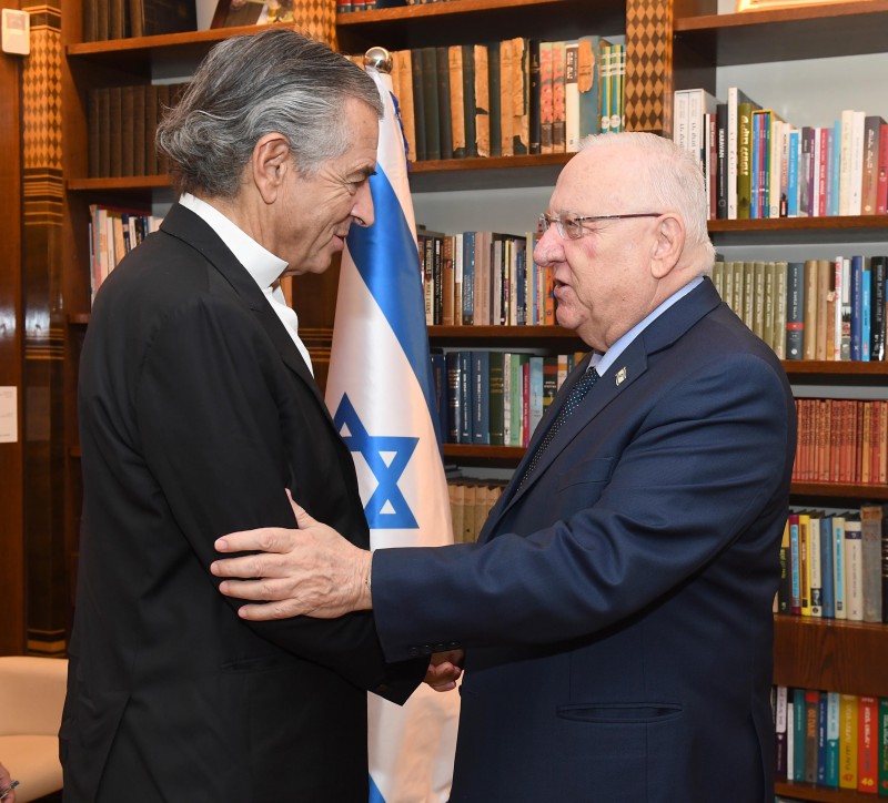Bernard-Henri Lévy et Reuven Rivlin, ils se serrent la main devant une bibliothèque et un drapeau d'Israël