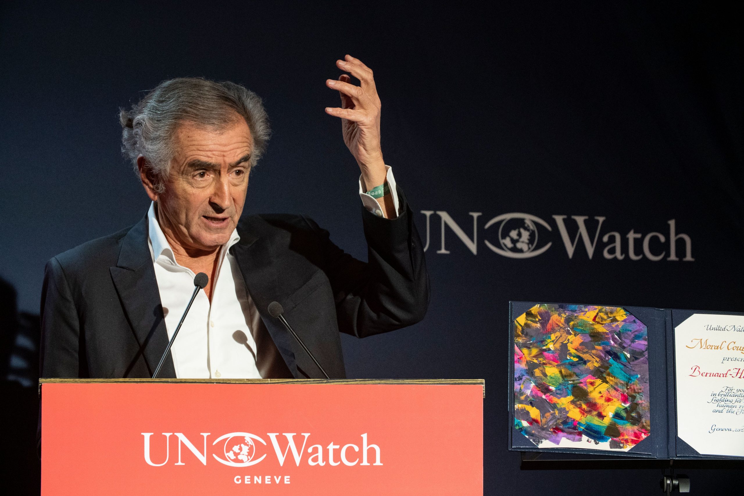 Bernard-Henri Lévy reçoit le Moral Courage Award lors du UN Watch Gala. Il est sur une estrade et prononce un discours derrière un pupitre avec un micro.
