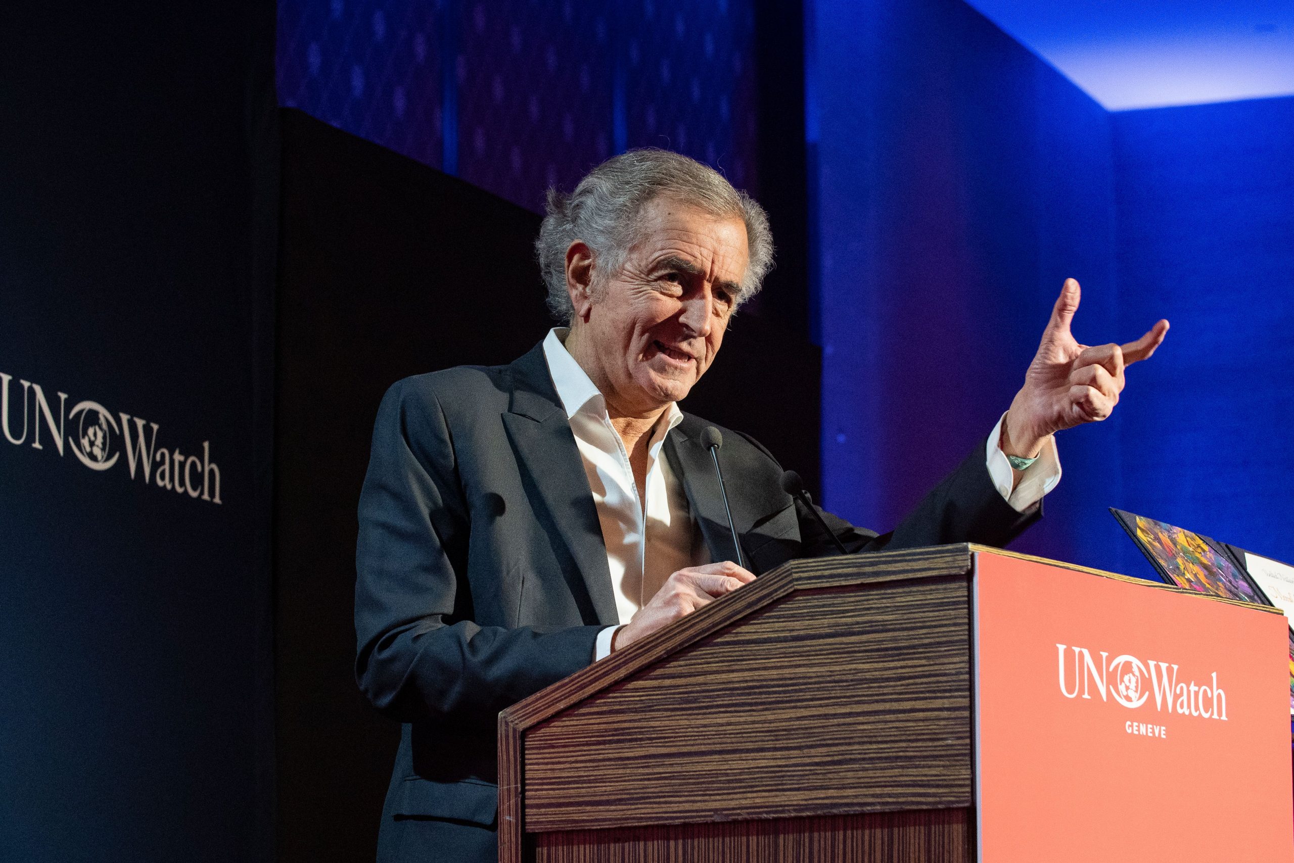Bernard-Henri Lévy reçoit le Moral Courage Award lors du UN Watch Gala. Il est sur une estrade et prononce un discours derrière un pupitre avec un micro.