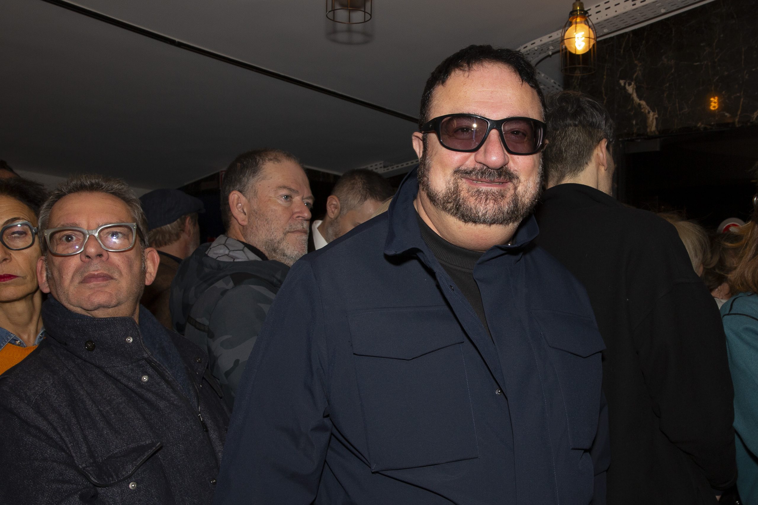 Éric Dahan dans les couloirs du cinéma, il est entouré par des membres du public et il porte des lunettes de soleil.