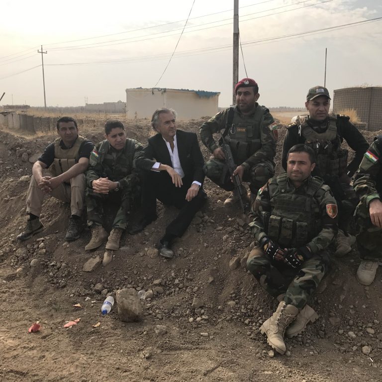 Bernard-Henri Lévy avec les Peshmergas, sur front du Kurdistan irakien, lors de la bataille de Mossoul. BHL est assis par terre avec sept soldats en uniforme.