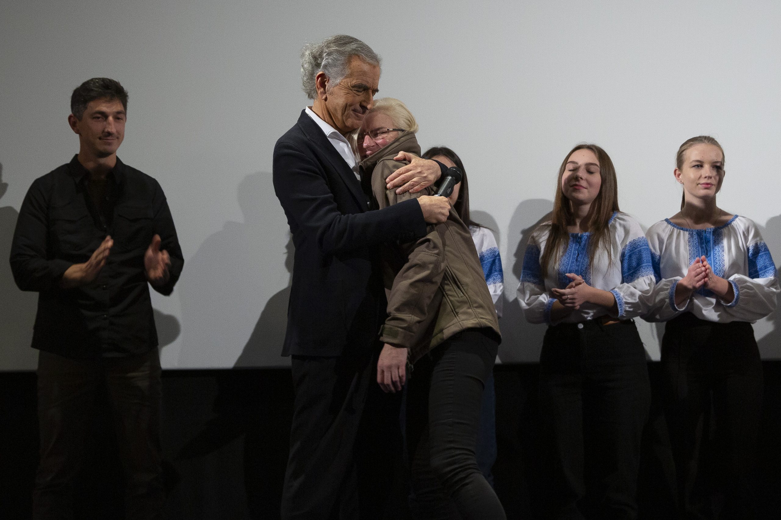 Taïra et Bernard-Henri Lévy se prennent dans les bras sous le regard de Vitaly Paly et de trois jeunes filles sur la scène du cinéma Le Balzac