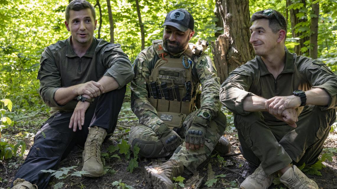 Trois militaires en uniformes sont assis par terre dans la fôret