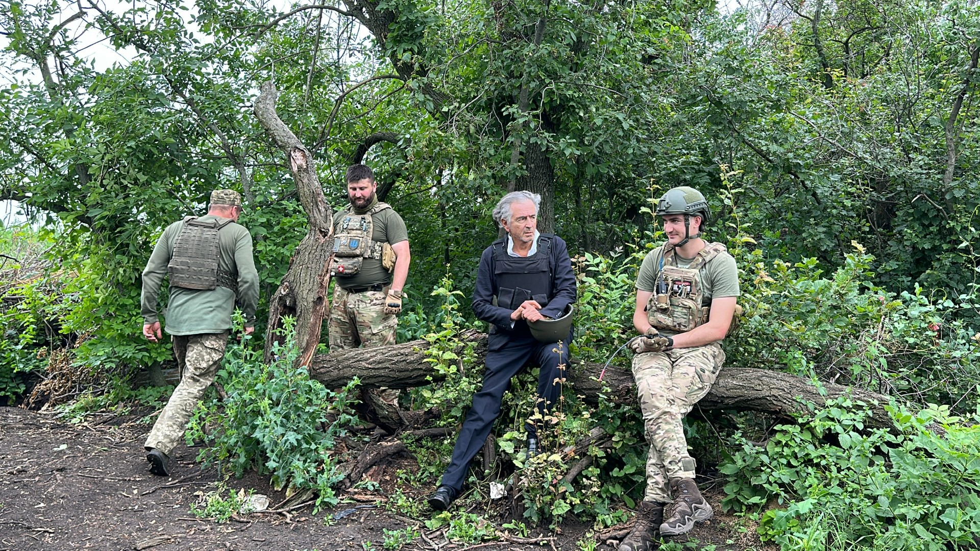Aux alentours de Bakhmout, BHL est avec les soldats ukrainiens, à quelques mètres des lignes russes. Ils sont dans la campagne, en pleine nature, assis sur un tronc d'arbre au milieu des feuillages.