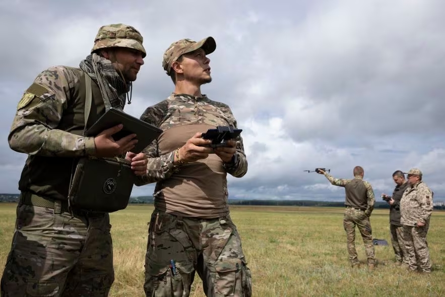 Sur cette base militaire, près de Kharkiv, des volontaires étrangers forment le Groupe Trident, on voit cinq militaires un uniforme dans une rase campagne ukrainienne.
