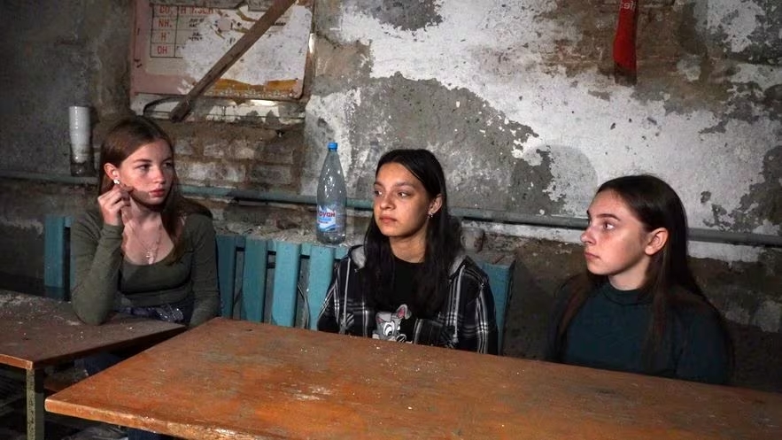 Trois jeunes filles assises derrière une table dans une cave délabrée