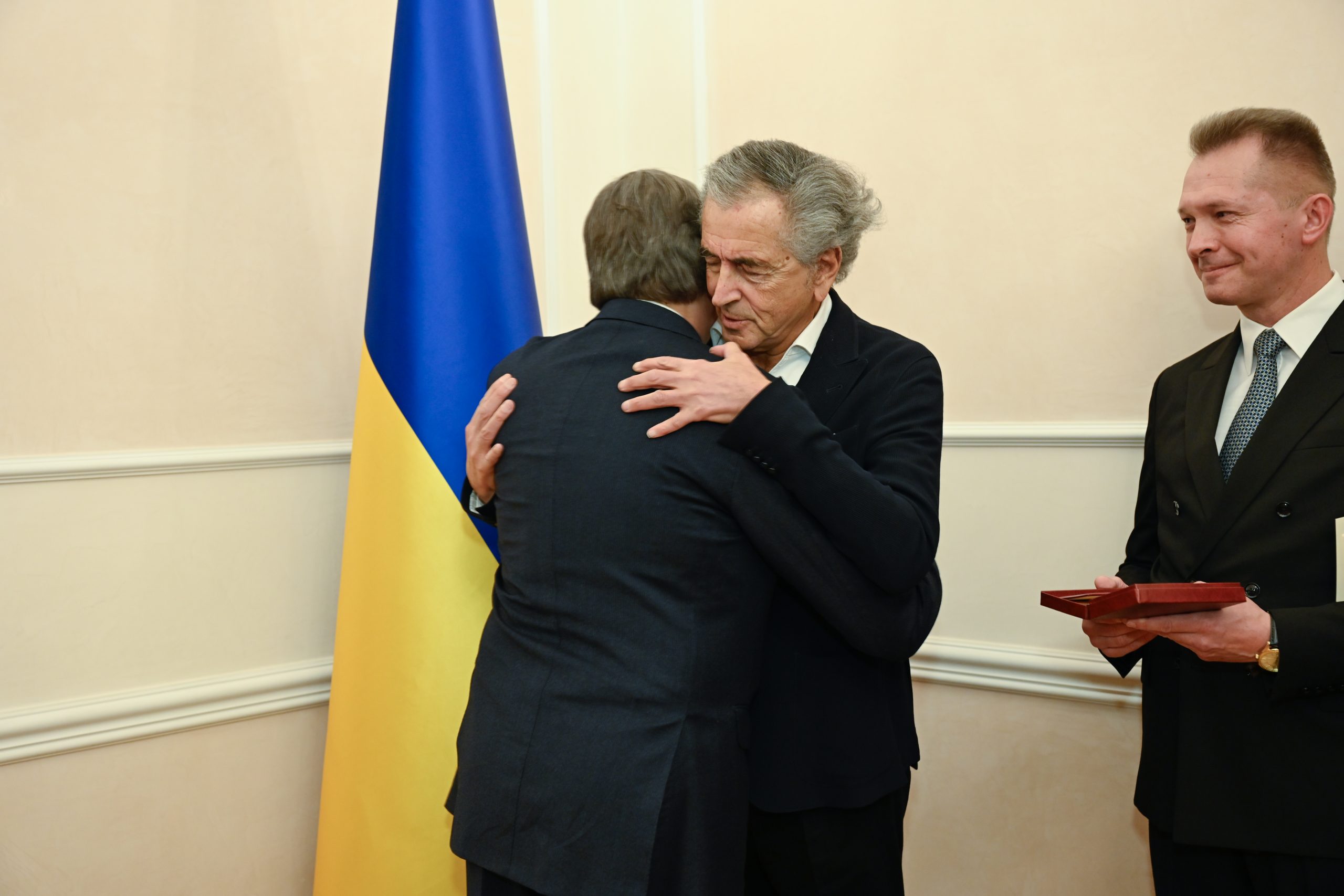 Vadym Omelchenko, ambassadeur d'Ukraine en France, remet l'insigne de Chevalier de l'Ordre du Mérite d'Ukraine à Bernard-Henri Lévy. Ils se prennent dans les bras devant un drapeau ukrainien.