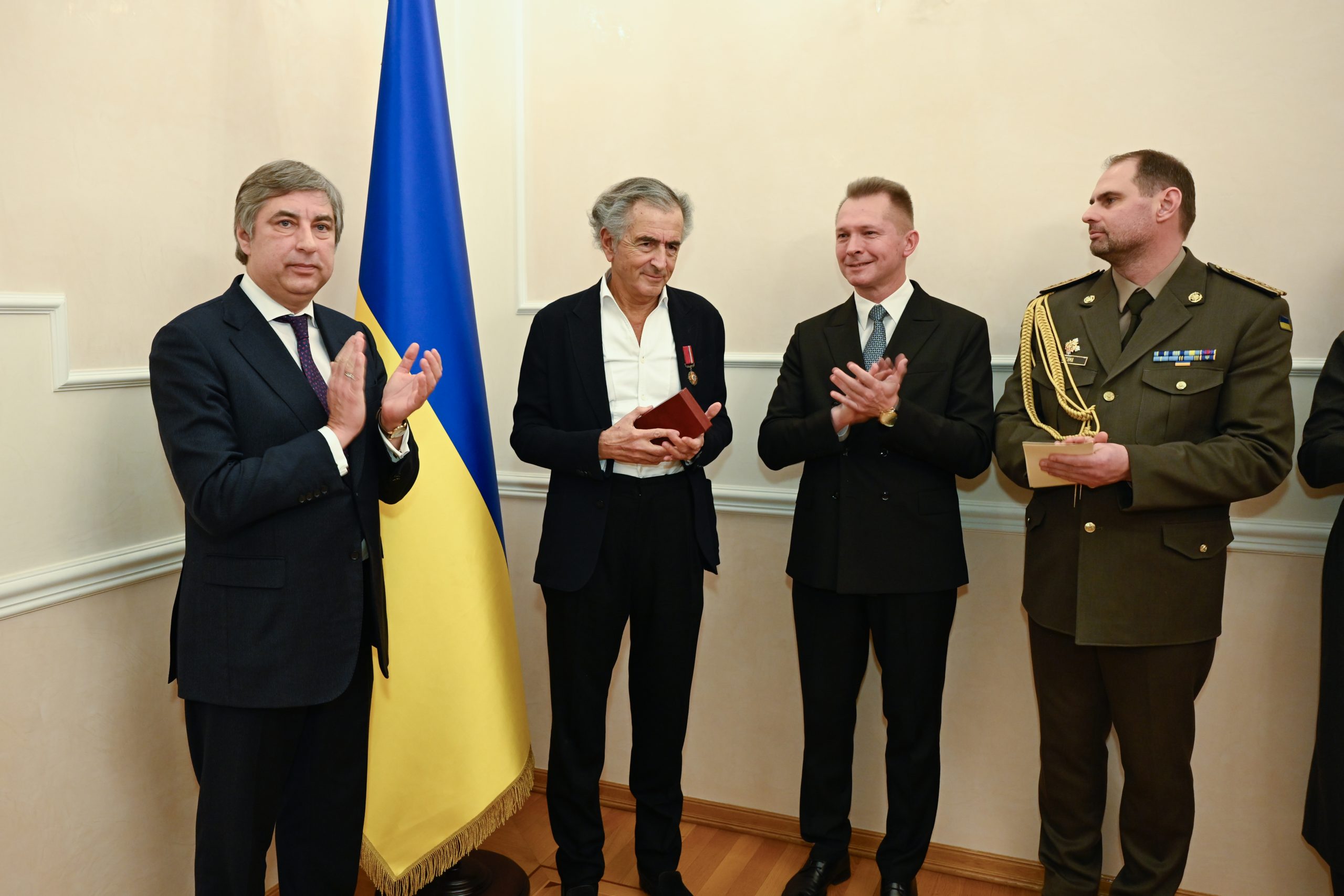BHL vient de recevoir l'insigne de Chevalier de l'Ordre du Mérite d'Ukraine. À ses côtés, Vadym Omelchenko, ambassadeur d'Ukraine en France. Ils sont devant un drapeau ukrainien`