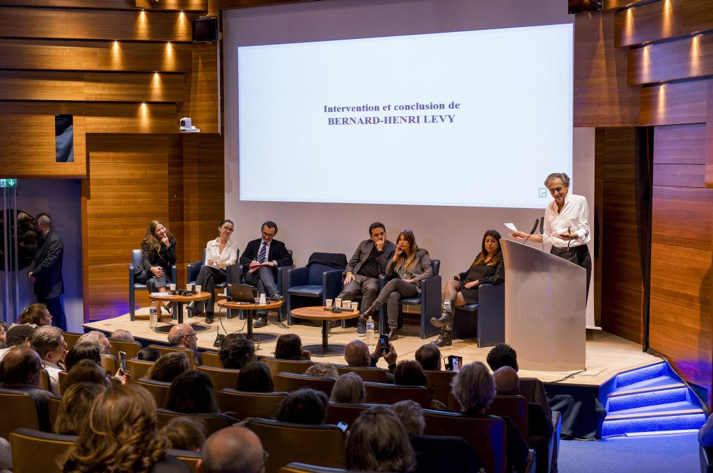 BHL parle derrière un pupitre sur la scène de l'auditorium de la Maison du Barreau, devant les co-Présidentes de la Commission ouverte Paris Israël du Barreau de Paris, et un collectif d'avocats.