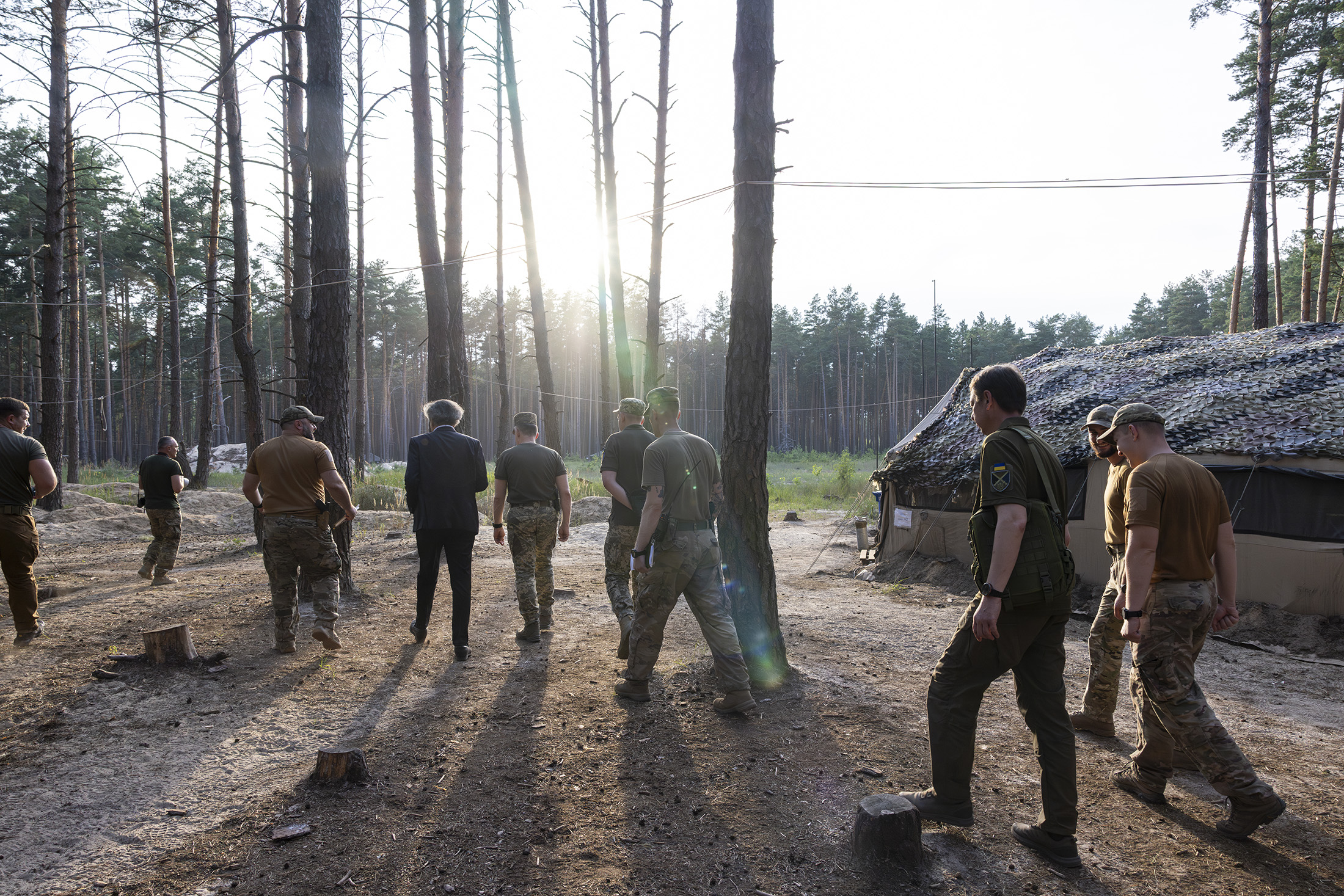 Bernard-Henri Lévy visite un camp militaire, dans une forêt au nord de Kharkiv. Il est entouré oar des soldats.